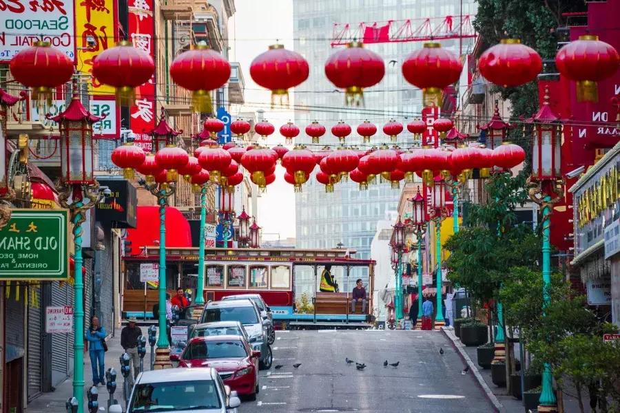 Se muestra una calle montañosa en el barrio chino de San Francisco con faroles rojos colgando y un tranvía pasando.