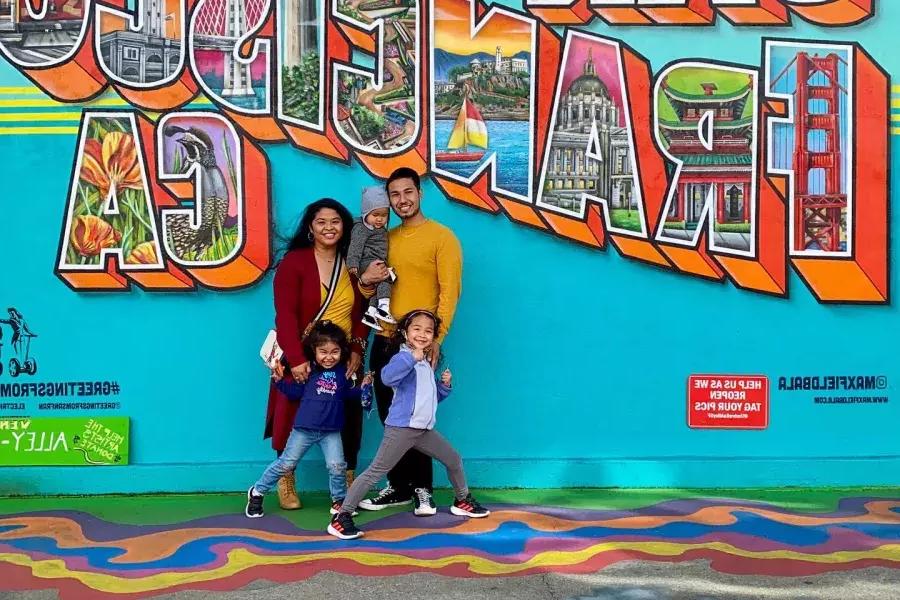 A family posing for a photo in front of a San Francisco mural